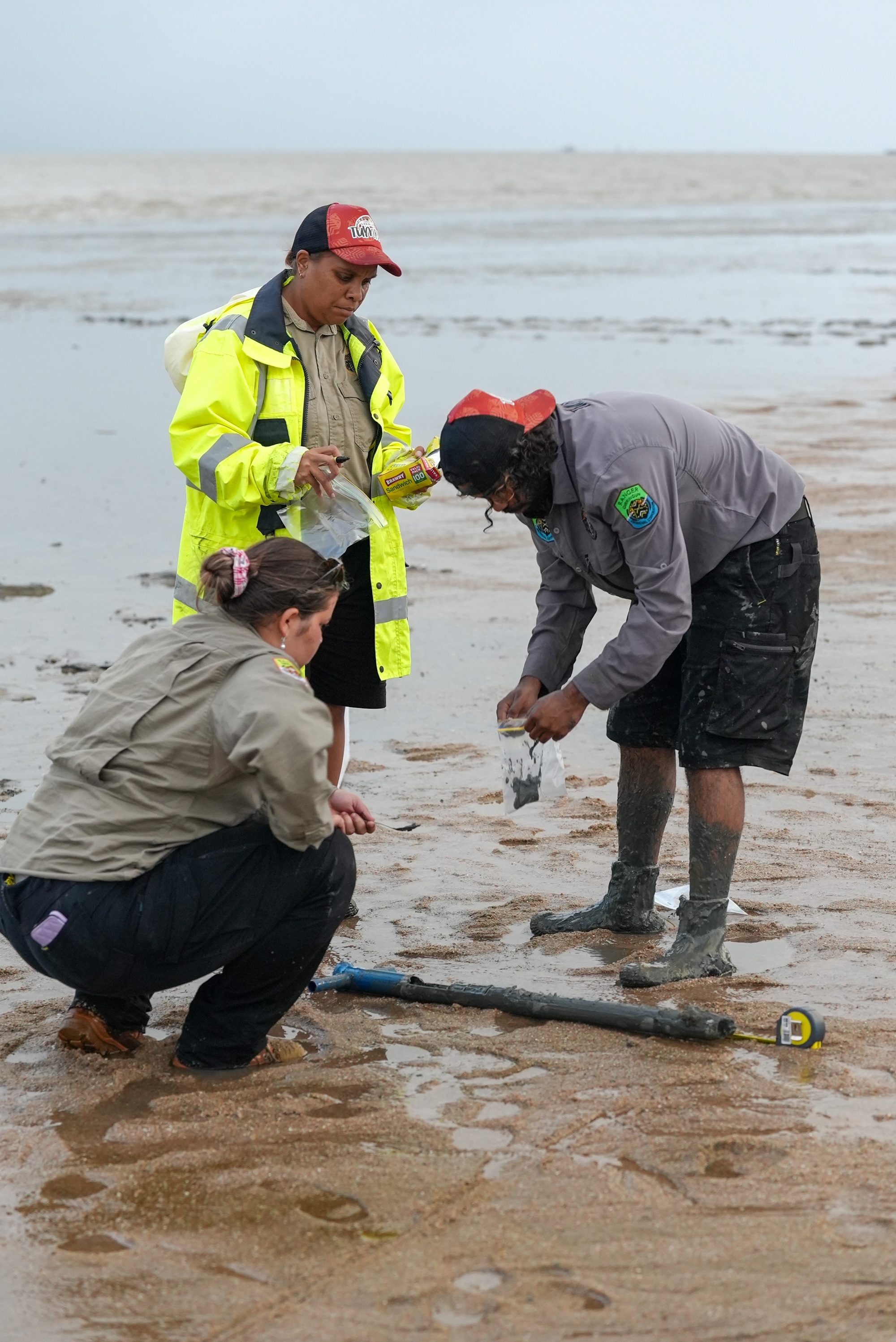 three poeple collect mud from a muddy beach