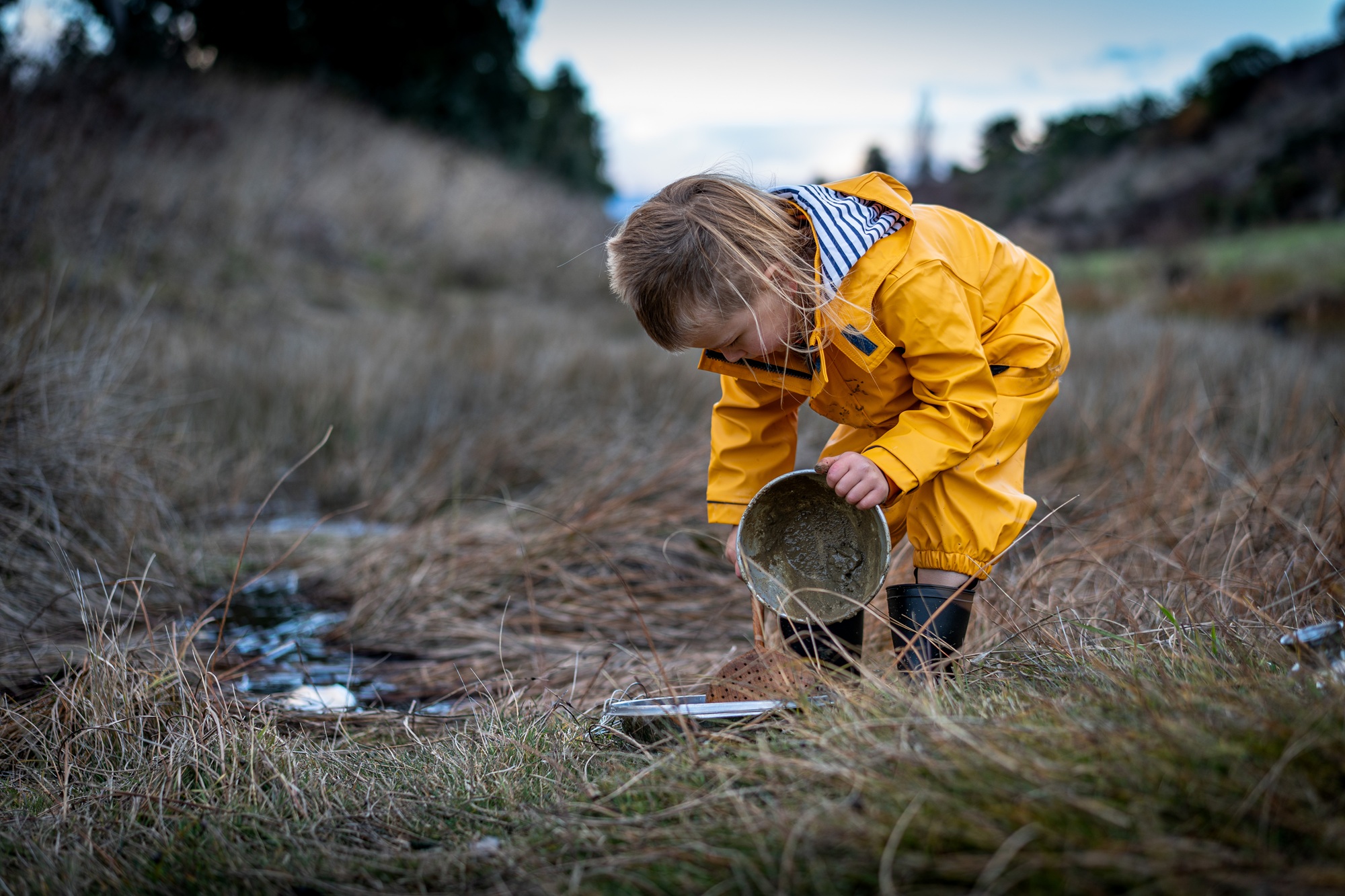 A child holds a bucket playing in mud.